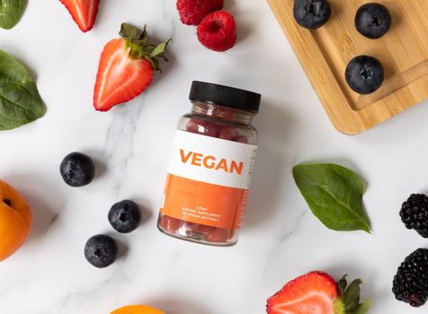 A flat lay of vegan supplements surrounded by fresh fruits on a white marble surface.
